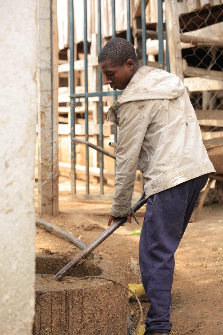 A young man mixing slurry at the inlet of a biogas digester beside a cattle shed in Rukungiri