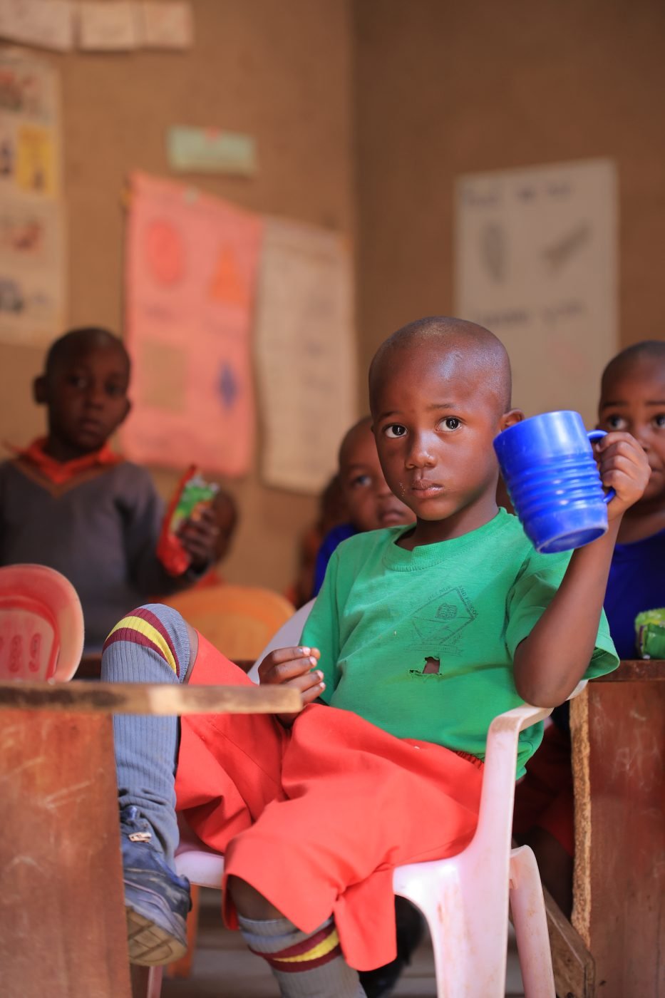 A pupil holding his cup at mealtime in a classroom in Rukungiri