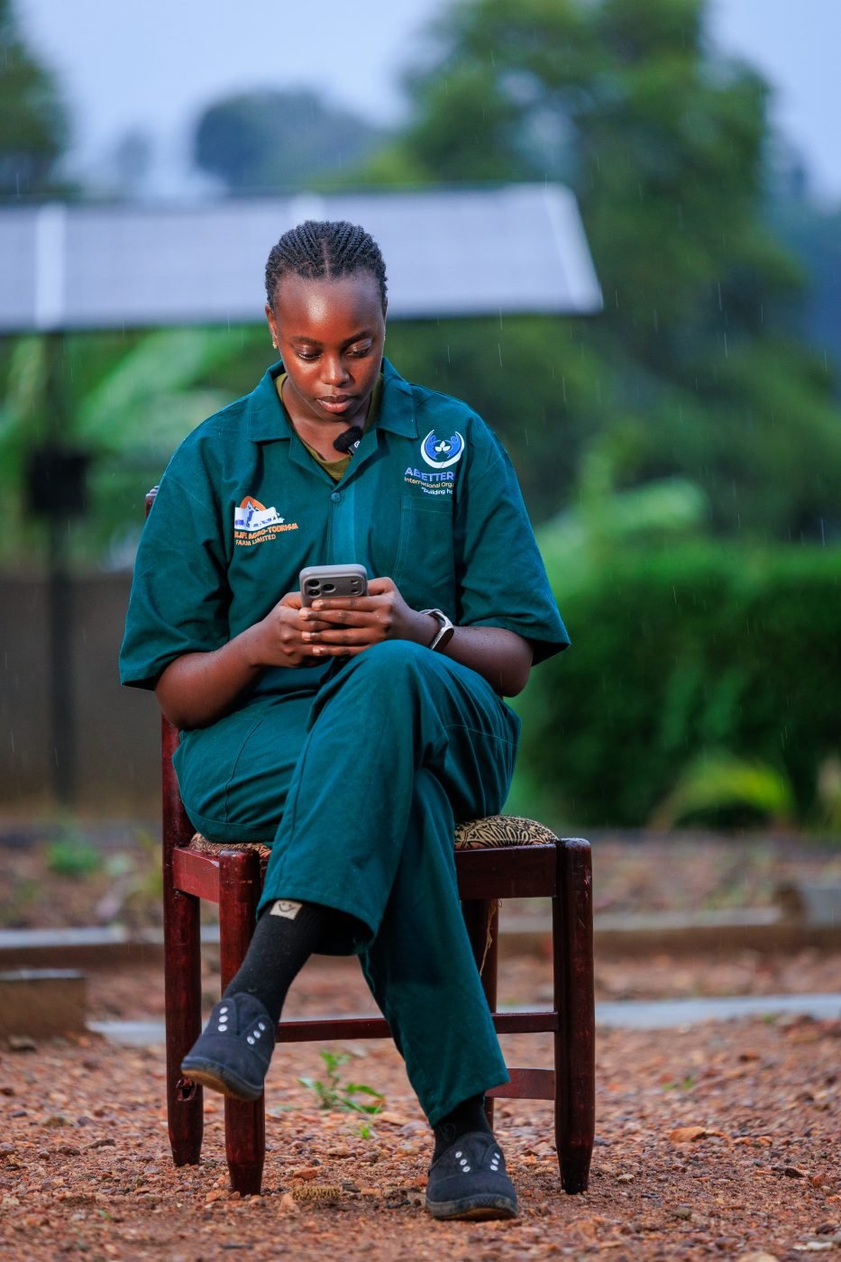 A young woman using her phone beside a solar panel in Rukungiri