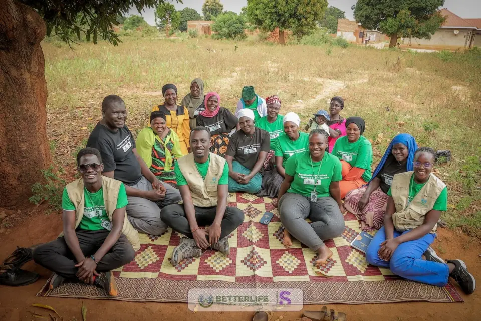 BetterLife team members sitting together on a mat with women from the community, under a tree