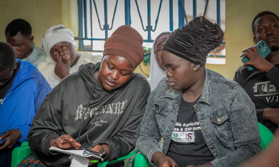 Two participants checking their phones during a training session in Yumbe