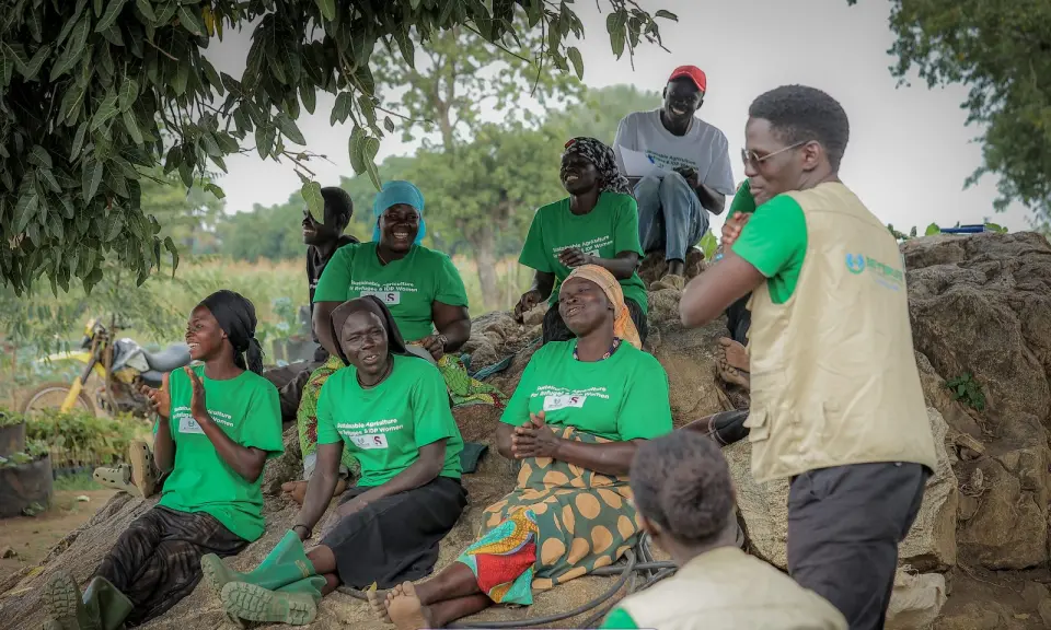 Women laughing as a BetterLife trainer teaches beside their sack gardens in Yumbe