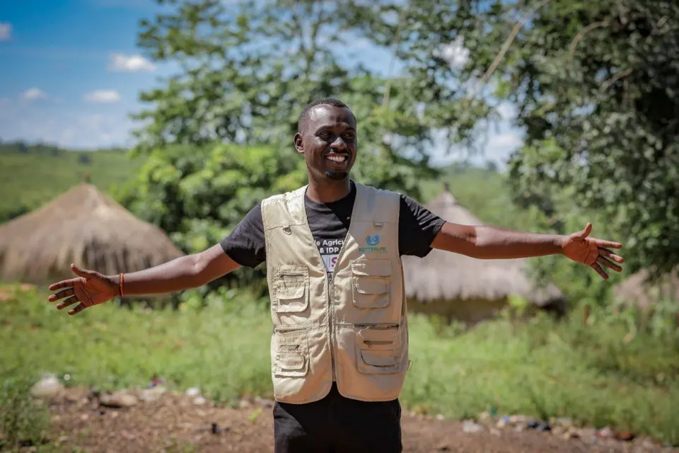 Edwin Namakanga, our Outreach Coordinator, greeting with open arms beside thatched homes