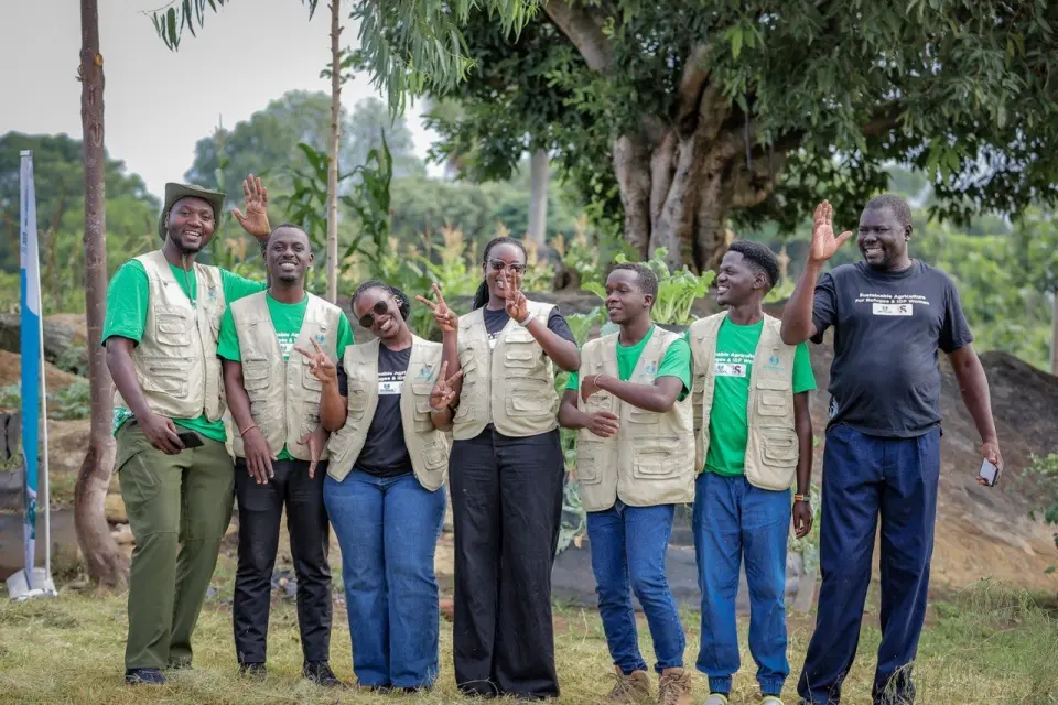 Eight BetterLife team members in programme vests, smiling and waving in a garden